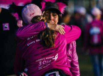 a woman in a pink shirt hugging another woman