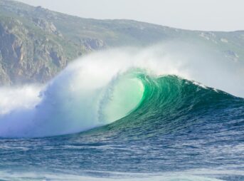 a large wave is breaking in front of a mountain