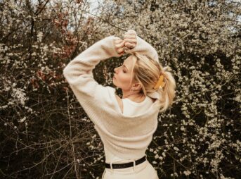 a woman standing in front of a bush with her hands on her head