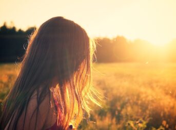 woman wearing black camisole top walking on grass field during sunrise